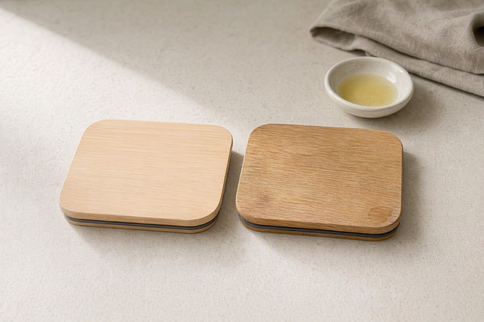 Two bamboo lids side by side, one new and pale, one darkened and slightly raised in the grain after a year of use, with a dish of food-safe oil