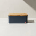 Kensington London charcoal steel bread box with bamboo board lid and red shield badge on pale limestone