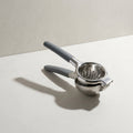Kensington London stainless steel lemon squeezer with grey grips and shield emblem on pale limestone
