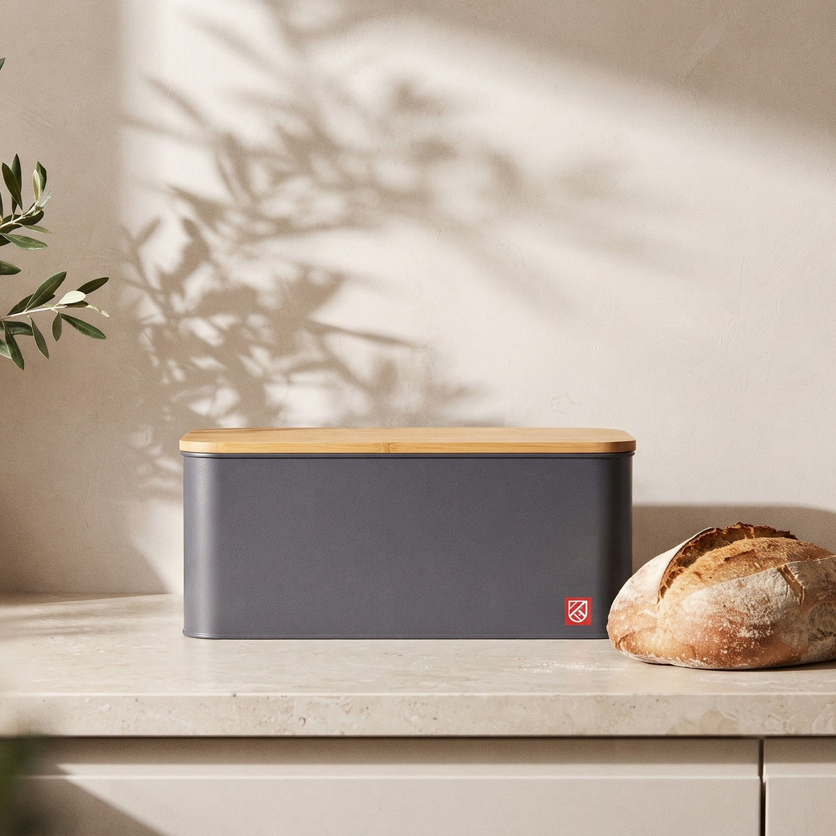 Bread box closed on a kitchen counter beside a sourdough loaf