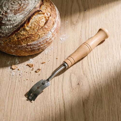 Bread lame on an oak worktop beside a scored sourdough loaf