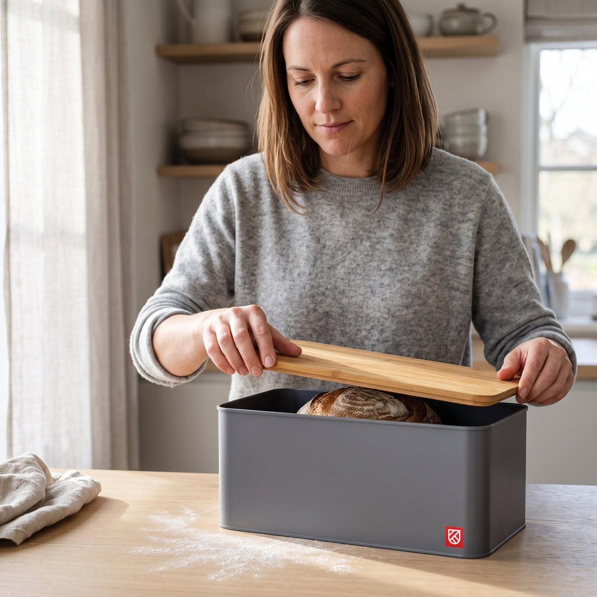 Lifting the bamboo lid off the bread box to reveal a sourdough loaf